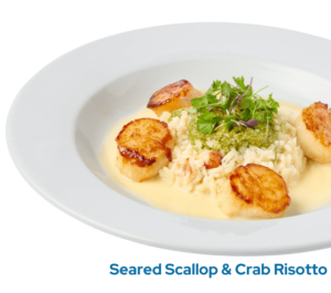 Seared jumbo scallops, crab risotto, tomatoes, parmesan cheese, basil pesto, beurre blanc on a plate with the caption Seared Scallop & Crab Risotto