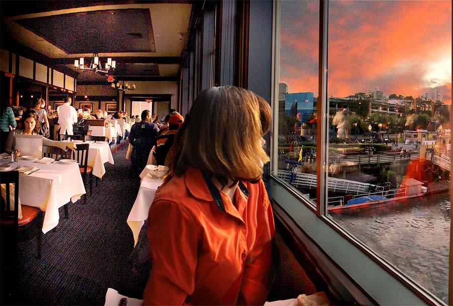 Woman seated at a restaurant table is looking at the sunset