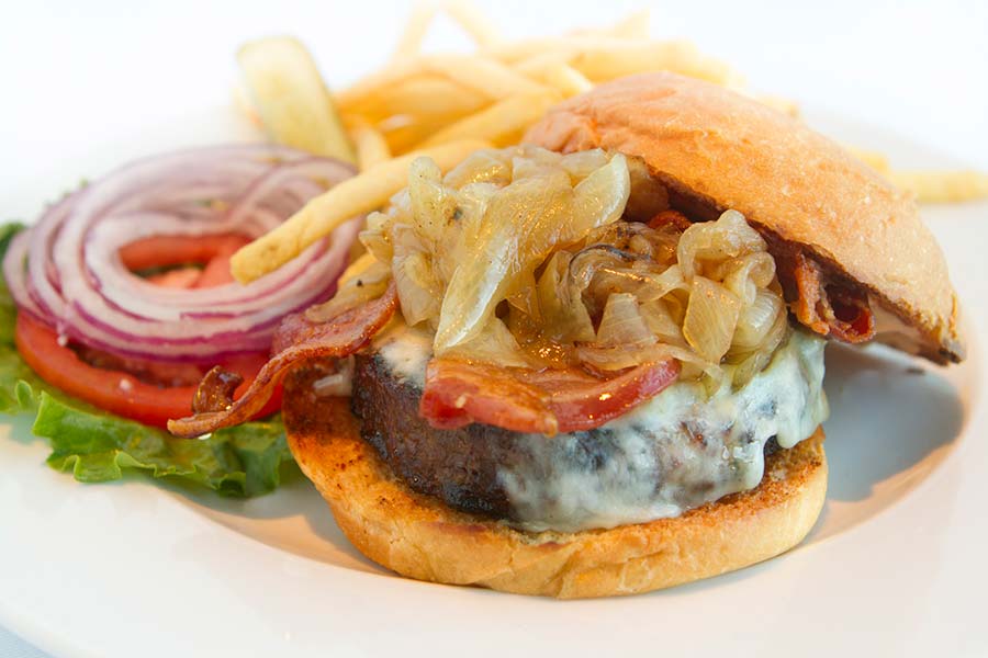 A hamburger with grilled onions on the meat and other fillers to the side